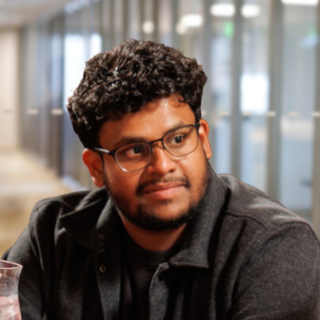 Headshot of Marut Patel, a smiling South Asian man with dark, curly hair, a beard, and glasses. He wearing is a dark jacket and shirt.