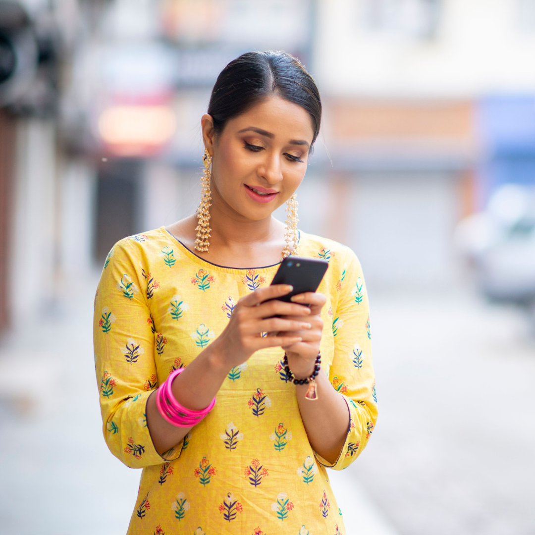 A smiling woman, with dark hair pulled back, is looking down at a smartphone and typing.