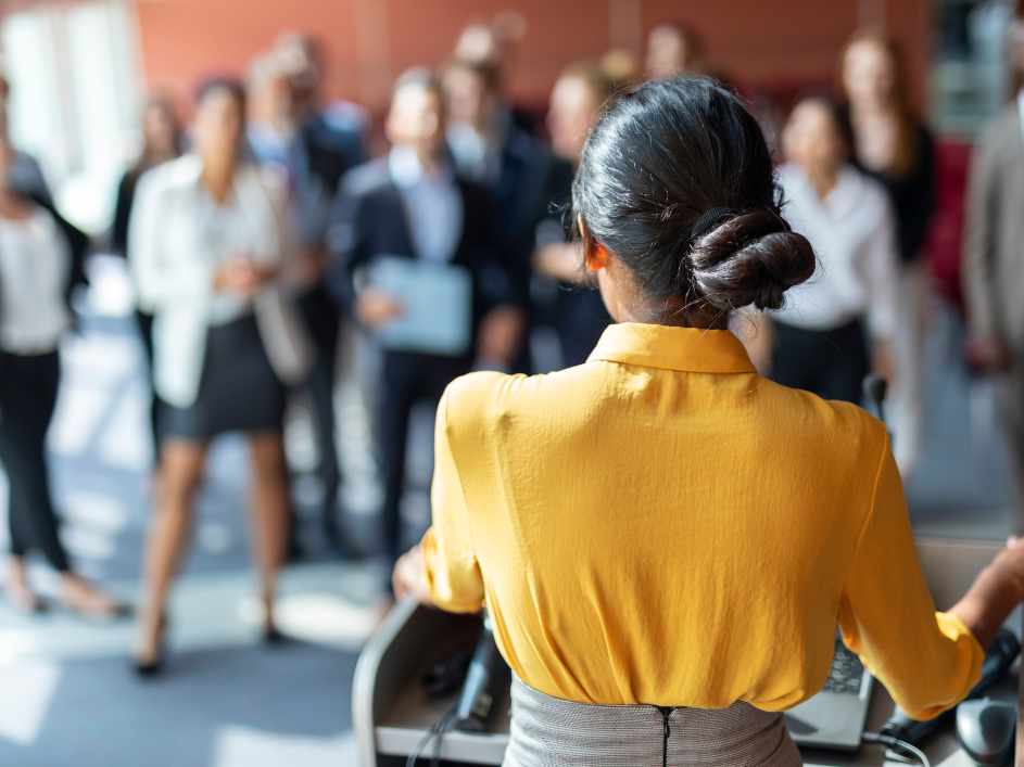 A professor speaks behind a podium to a group of students.