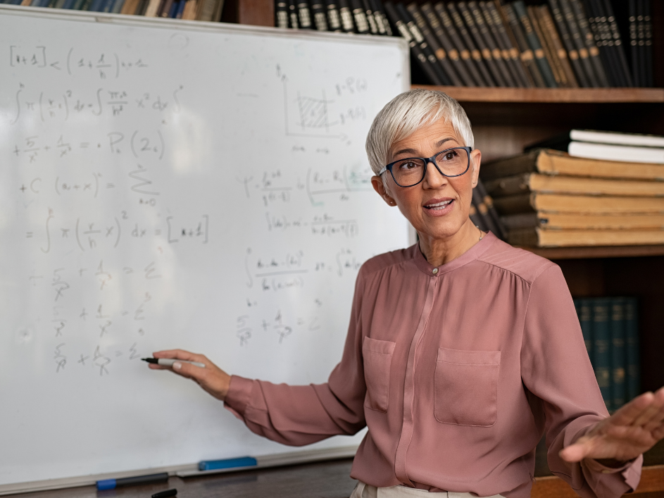 A female professor presents while gesturing to a whiteboard.