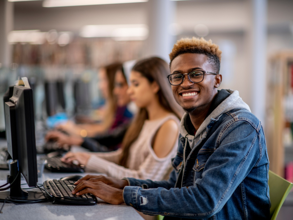 A PhD student smiles using a computer in a computer lab.