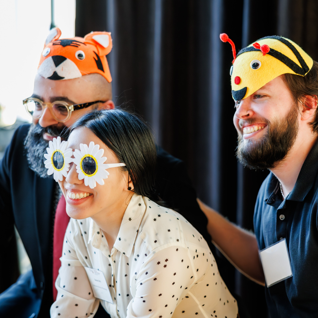Three PhD students wearing animal hats at a celebration event.