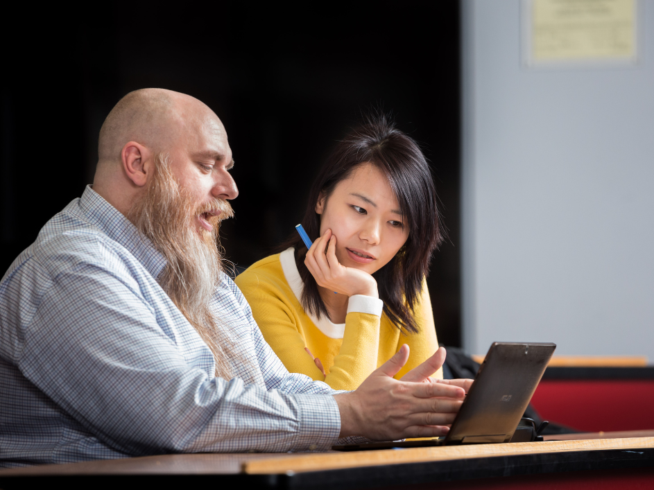 A DeGroote professor talking to doctoral student while gesturing to a laptop.