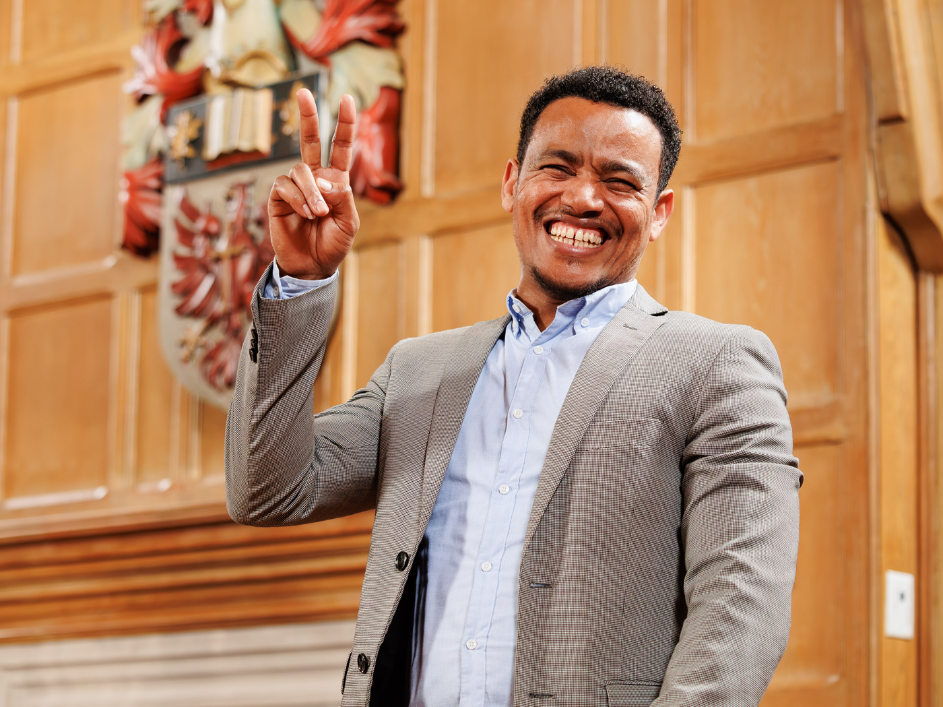A PhD student holding up a peace sign and smiling widely.