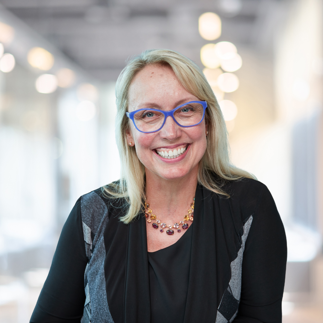Headshot of Milena Head, a smiling woman with blonde hair, glasses, wearing a dark top.
