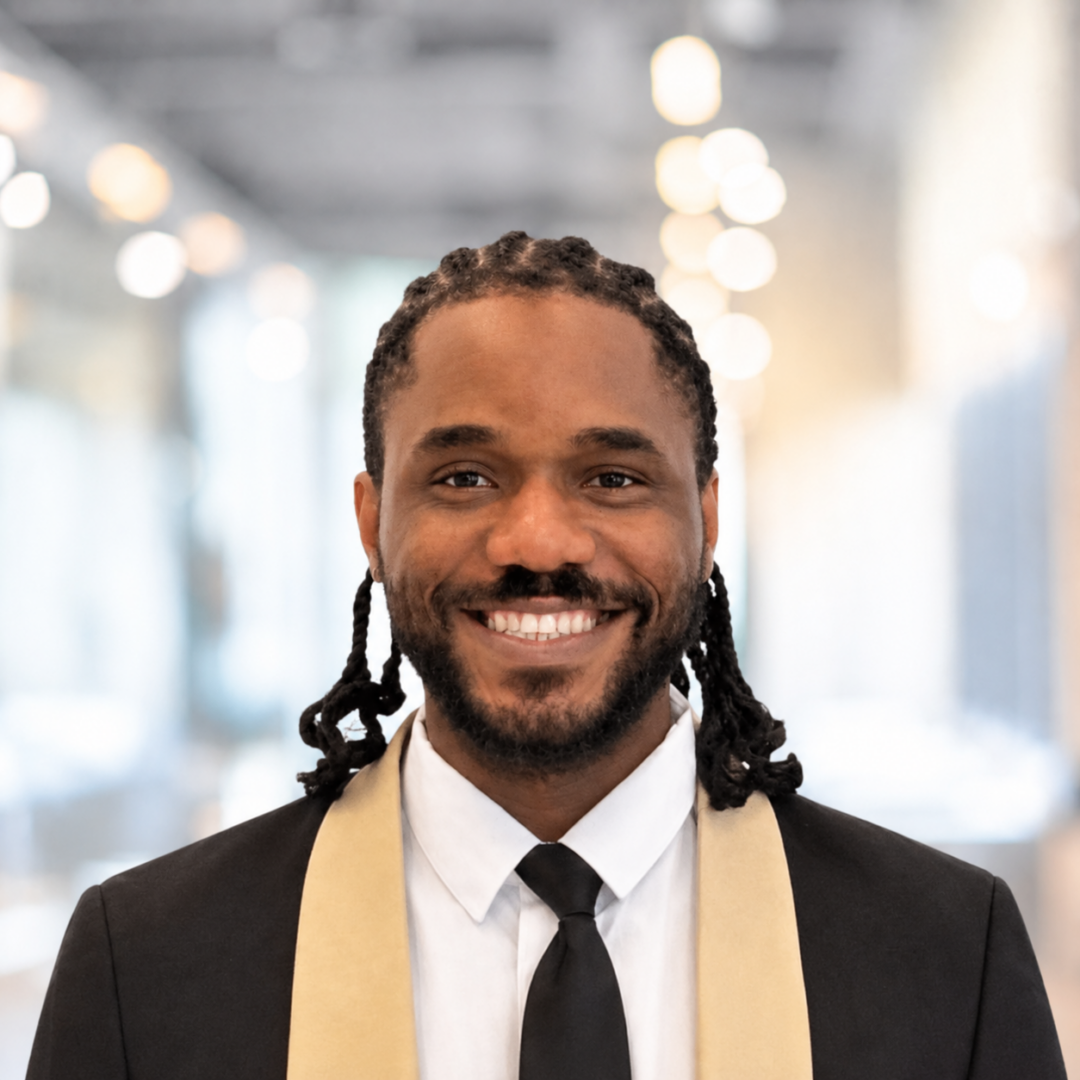 A headshot of Chinonso Anyaehie, a smiling man with dark braided hair, wearing a black suit, white shirt, and black tie.
